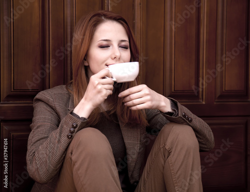 Style redhead girl drinking coffee near wood doors.