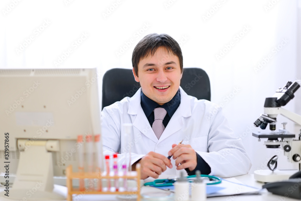 Smiling medical doctor sitting at table in office Smiling medical doctor sitting at table in office