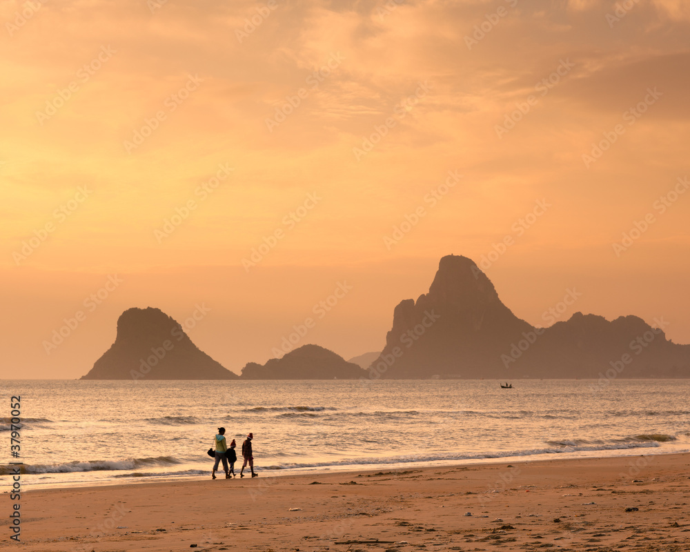 Happy family walking on the beach in the morning with golden sky color and mountain in background