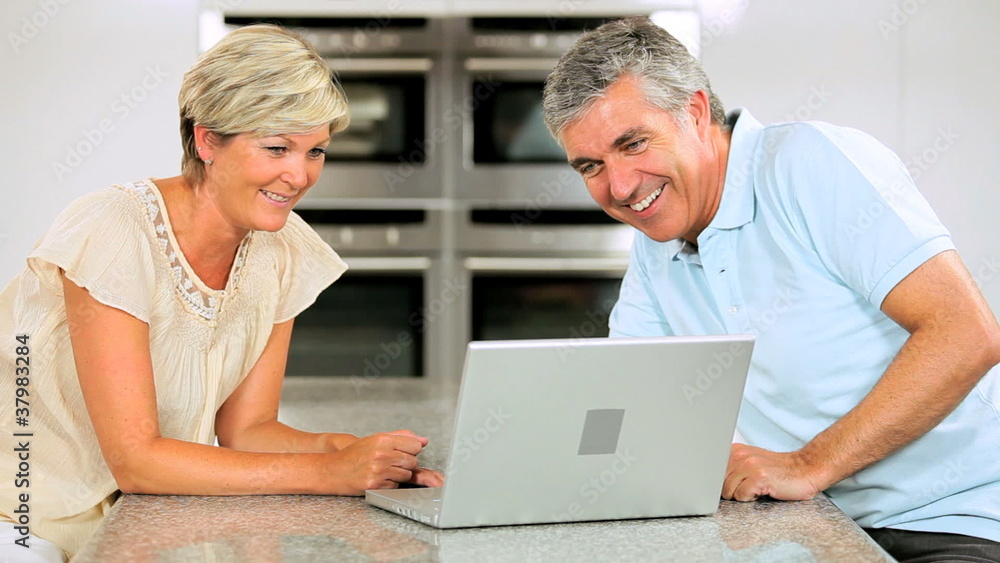 Mature Couple Using Wireless Latop in Home Kitchen Mature Couple Using Wireless Latop in Home Kitchen