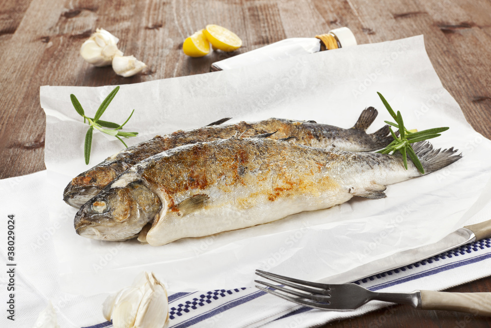 Two grilled trouts with fresh herbs and lemon pieces on wooden t Two grilled trouts with fresh herbs and lemon pieces on wooden t