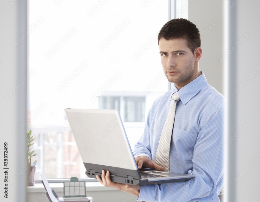 Young businessman standing with laptop in hand Young businessman standing with laptop in hand