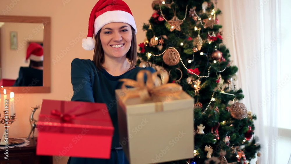 Happy woman offering gift boxes, christmas tree in background Happy woman offering gift boxes, christmas tree in background