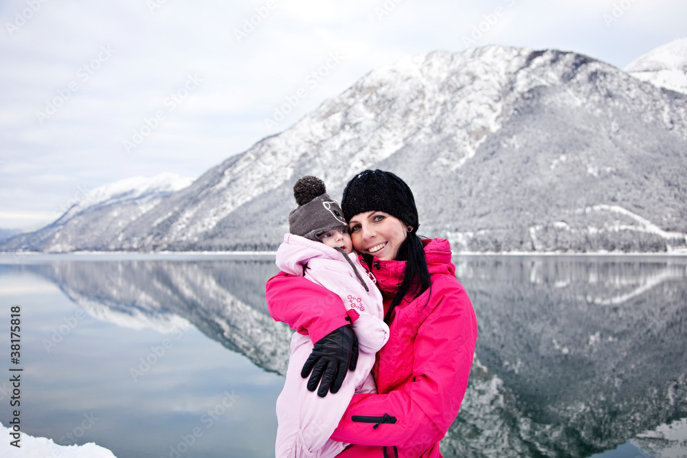 Glückliche Mutter mit Baby im Schnee am Achensee im Winterurlaub