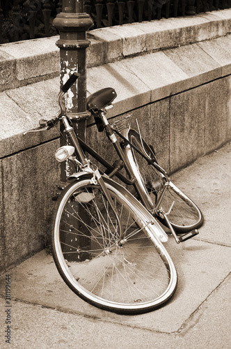Abandoned damaged bicycle locked to an iron pillar on sidewalk photo