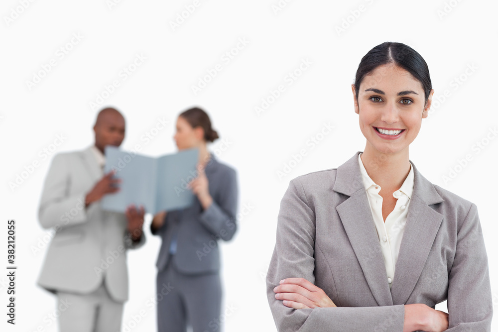 Smiling saleswoman with arms crossed and colleagues behind her Smiling saleswoman with arms crossed and colleagues behind her