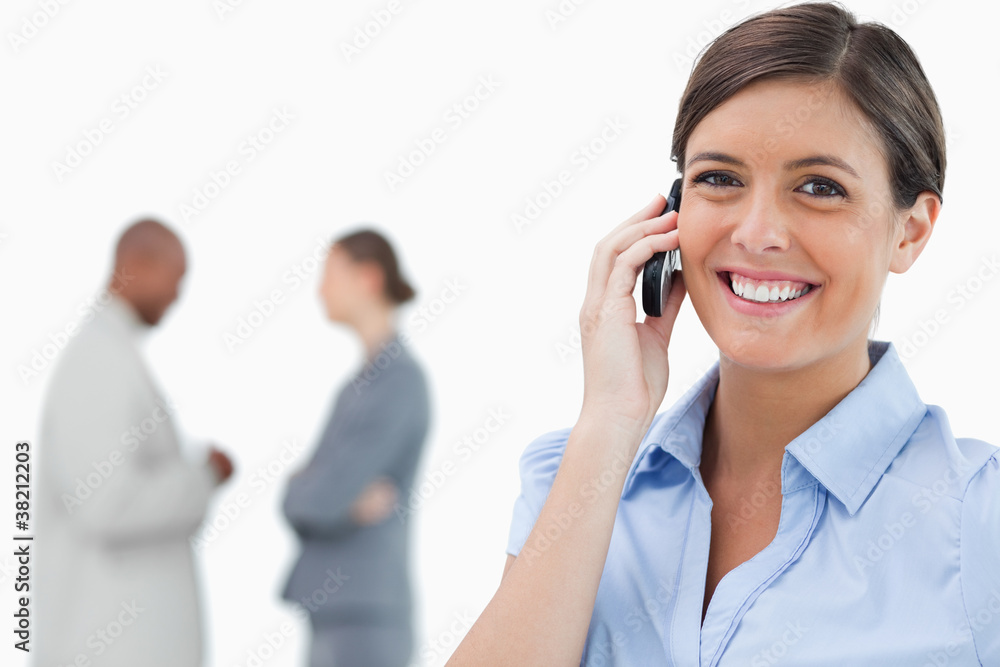 Smiling tradeswoman with mobile phone and co-workers behind her Smiling tradeswoman with mobile phone and co-workers behind her