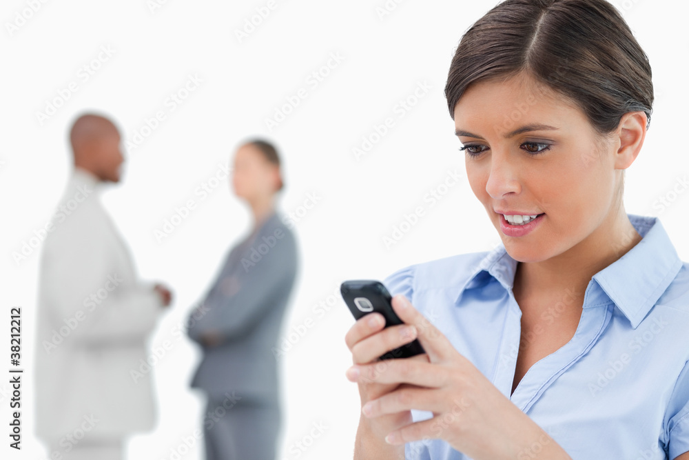 Businesswoman reading text message with associates behind her Businesswoman reading text message with associates behind her