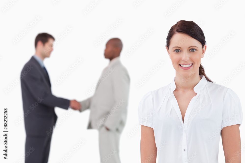 Smiling businesswoman with hand shaking trading partners behind Smiling businesswoman with hand shaking trading partners behind