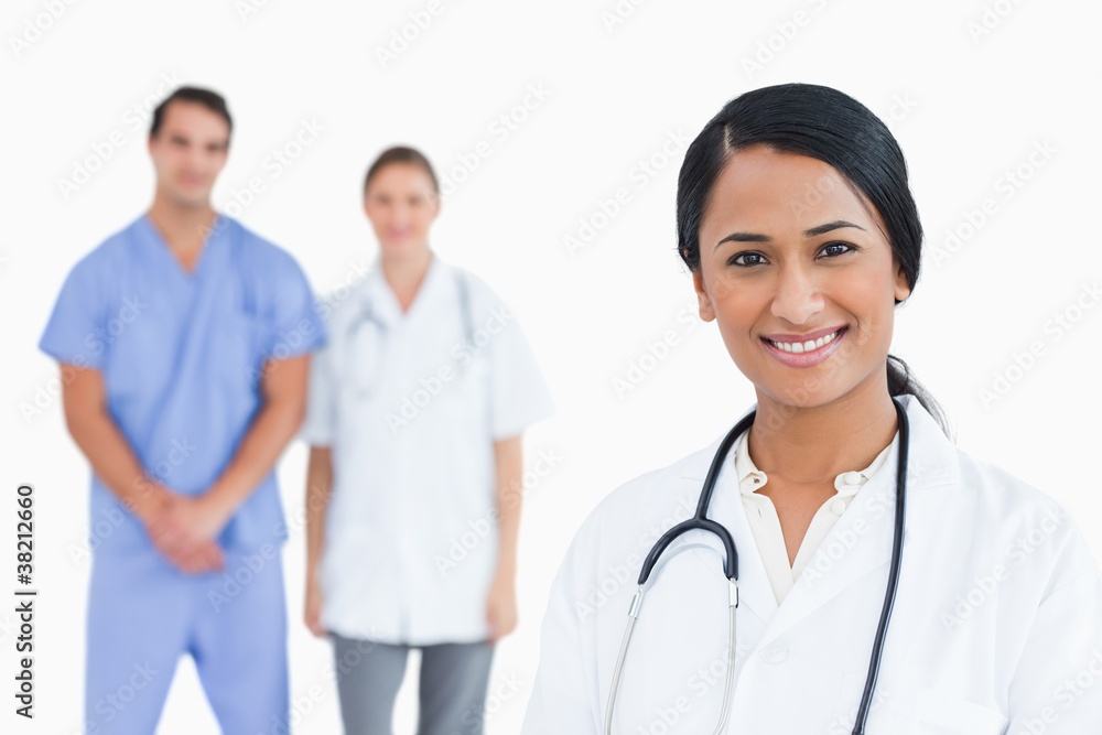Smiling doctor with colleagues behind her Smiling doctor with colleagues behind her