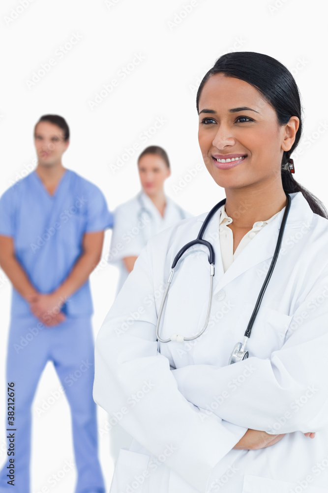 Smiling doctor with arms folded and colleagues behind her Smiling doctor with arms folded and colleagues behind her