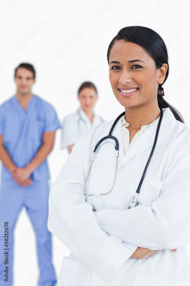 Smiling doctor with arms folded and staff behind her Smiling doctor with arms folded and staff behind her