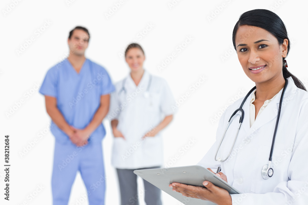 Doctor with notepad and colleagues behind her Doctor with notepad and colleagues behind her