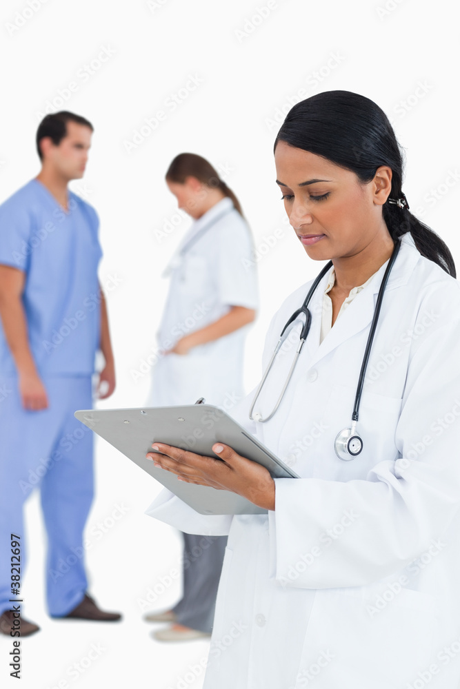 Doctor taking notes with staff members behind her Doctor taking notes with staff members behind her