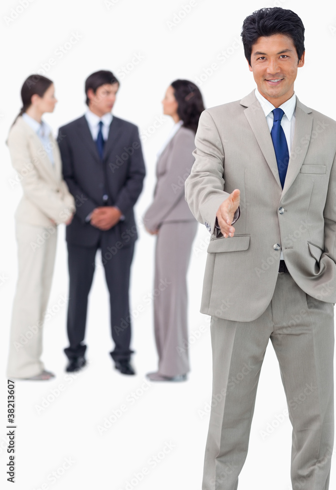 Businessman with team behind him offering hand Businessman with team behind him offering hand