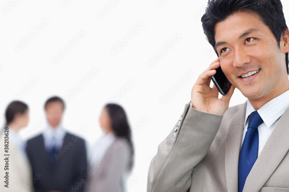 Smiling businessman on his mobile phone and team behind him