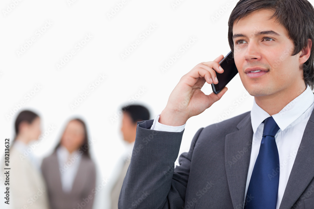 Salesman on his cellphone with team behind him Salesman on his cellphone with team behind him