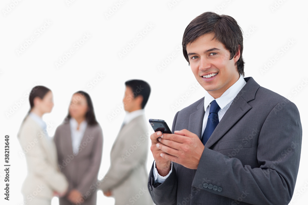 Salesman holding cellphone with team behind him Salesman holding cellphone with team behind him