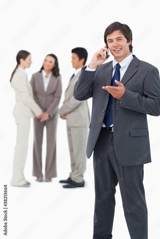 Salesman talking on cellphone with team behind him