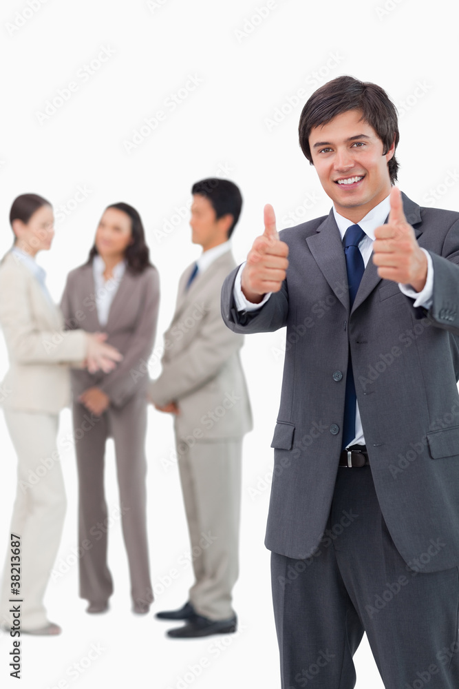 Salesman giving thumbs up with team behind him Salesman giving thumbs up with team behind him