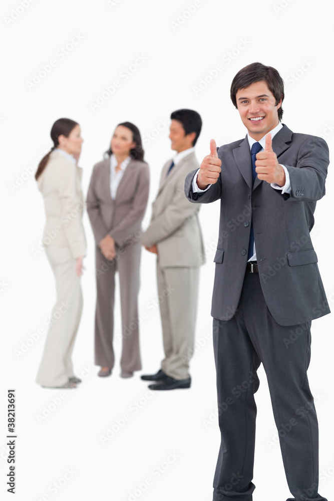 Salesman giving thumbs up with colleagues behind him Salesman giving thumbs up with colleagues behind him