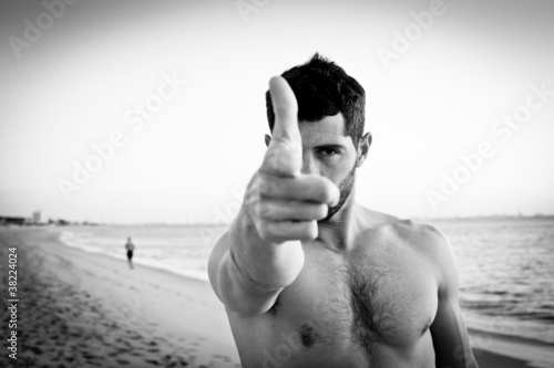 Muscular man on the beach pointing at camera. Black and white