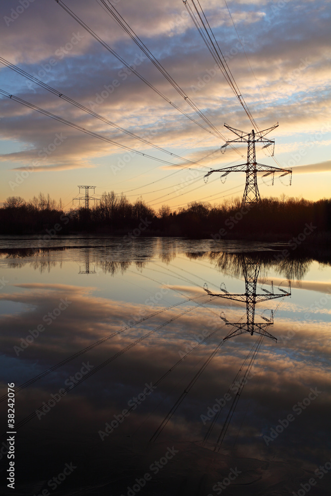 Electricity pylon with reflection in water at sunset