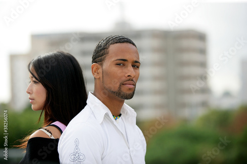 Tableau sur toile Young couple standing back-to-back on the outskirts of a city