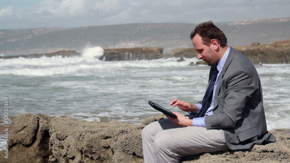 Businessman working on tablet computer on the rocks Businessman working on tablet computer on the rocks