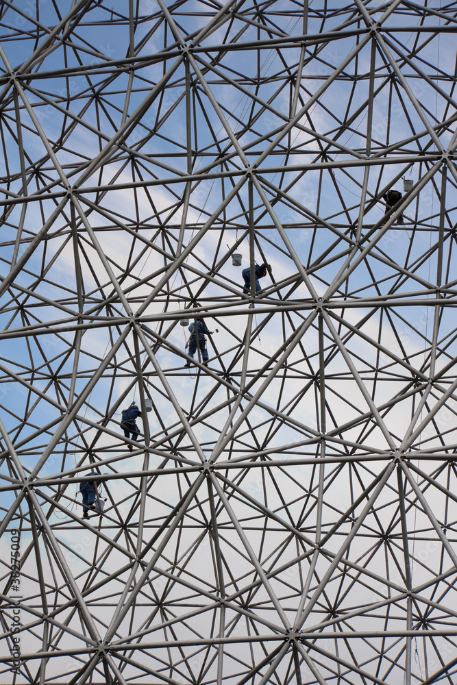 Climbers on a metallic net structure painting the sky.