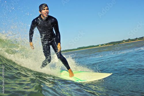 Young surfer smiles surfing wave in wetsuit sunny day