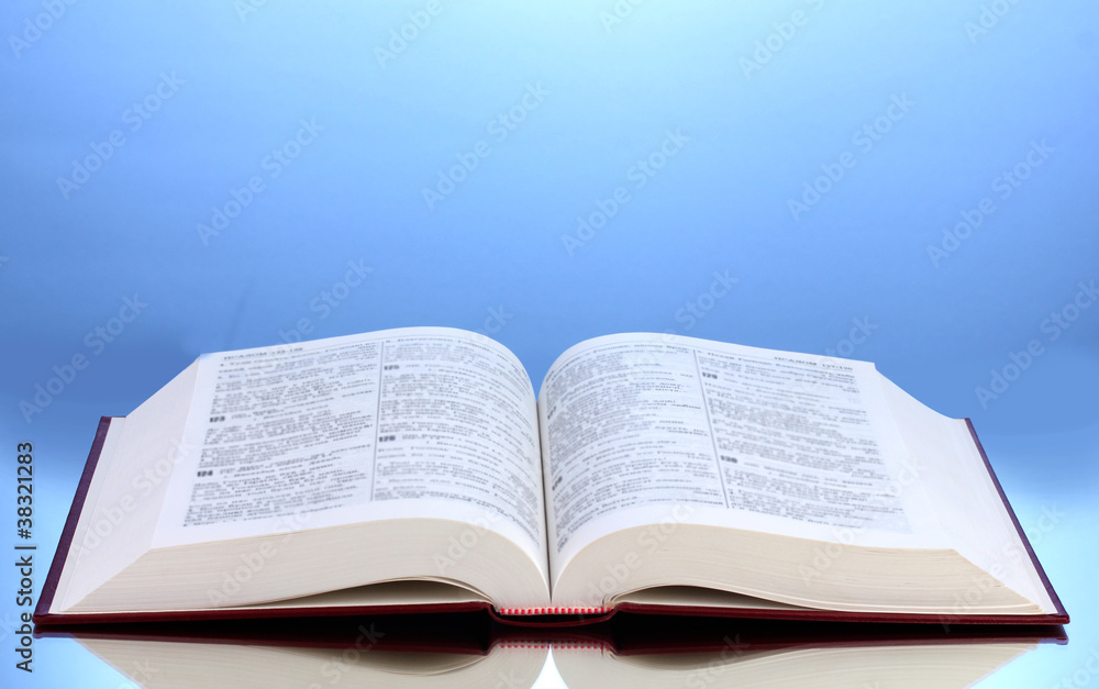 Fototapeta premium Open book on reflective surface of table on blue background