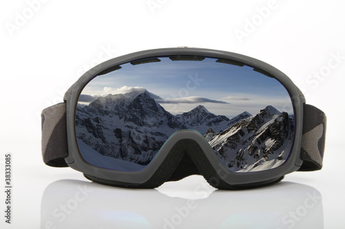 Skibrille auf weißem Untergrund mit Spiegelung eines Alpenpanoramas im Glas