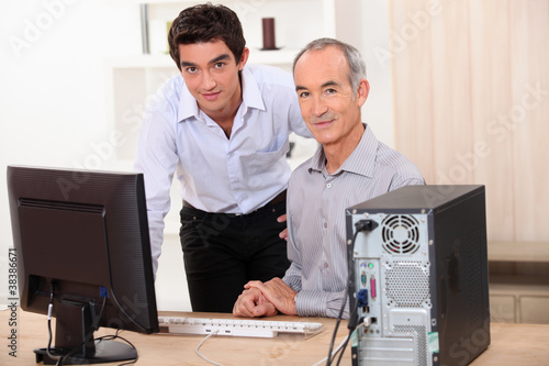 a young man and a senior man behind a computer photo