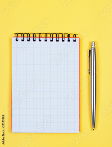 Notebook with pen on bright yellow background.