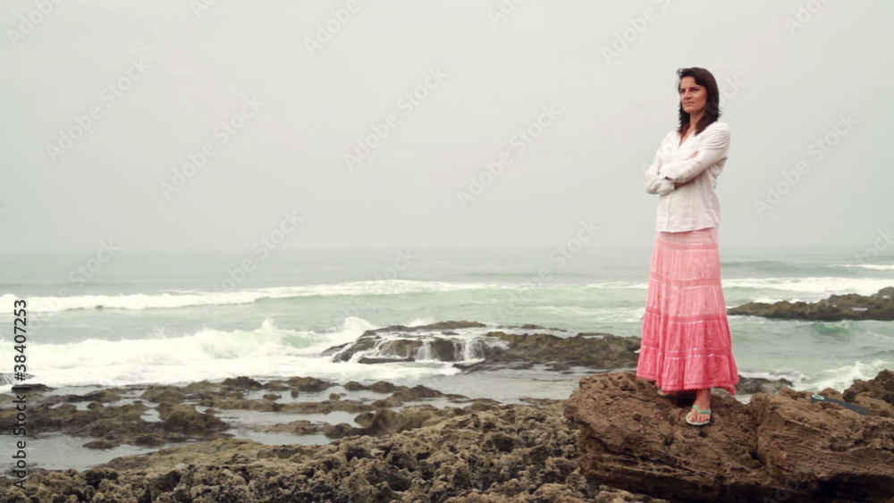 Pensive woman standing on rocks and looking at the sea Pensive woman standing on rocks and looking at the sea