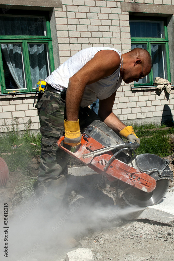 Worker with industrial saw cutting a concrete block Worker with industrial saw cutting a concrete block