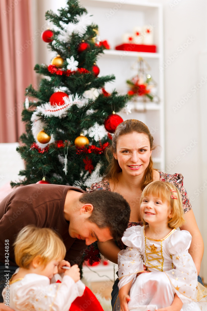 Parents with two daughters spending time near Christmas tree Parents with two daughters spending time near Christmas tree