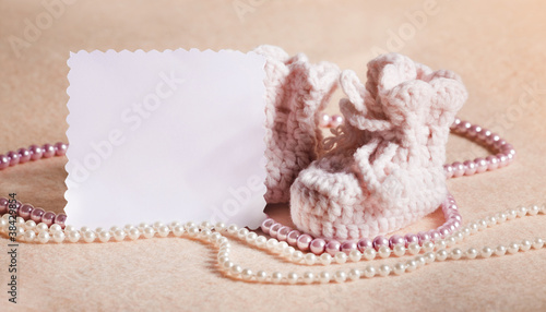 Pink baby shoes with blank card on peach background