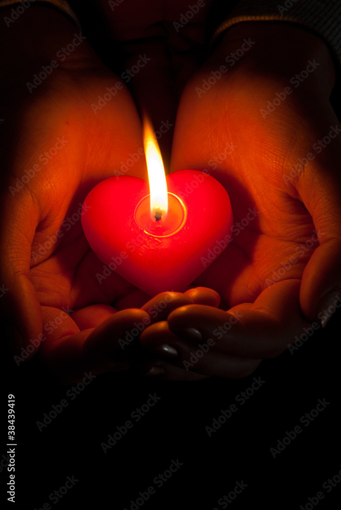 Human hands hold heart shaped burning candle