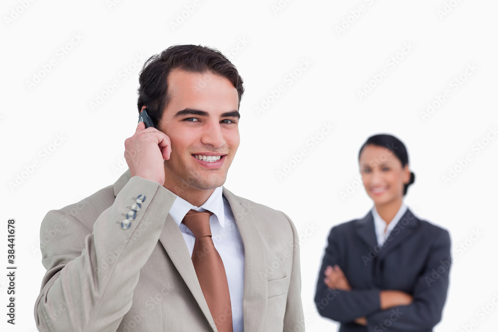 Smiling salesman on his cellphone with colleague behind him Smiling salesman on his cellphone with colleague behind him