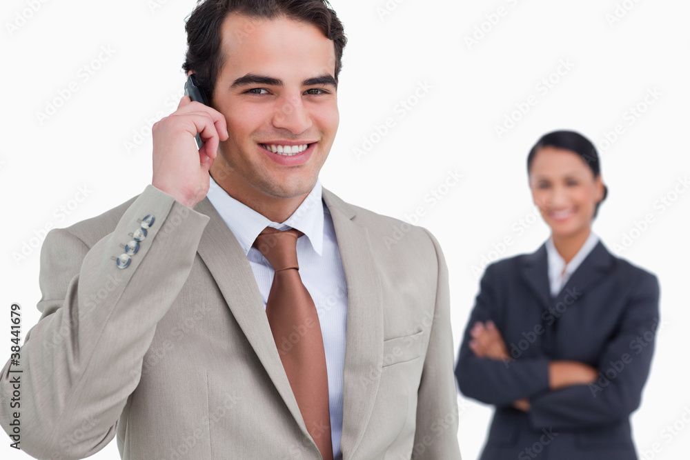 Salesman on his cellphone with colleague behind him Salesman on his cellphone with colleague behind him