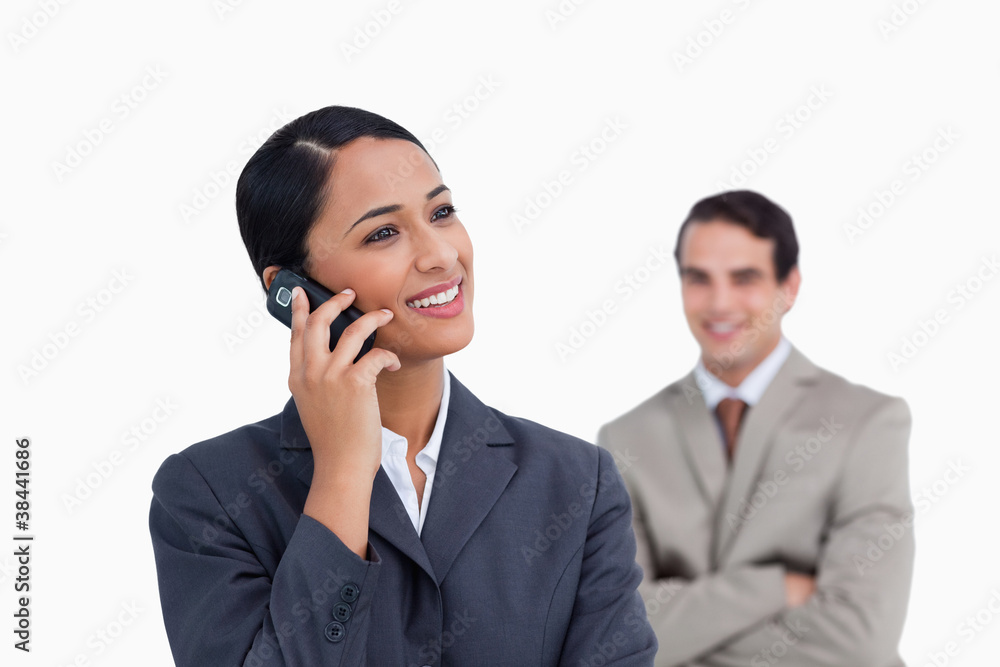 Smiling saleswoman on her mobile phone and co-worker behind her Smiling saleswoman on her mobile phone and co-worker behind her