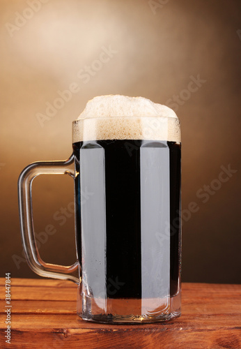 dark beer in a mug on wooden table on brown background