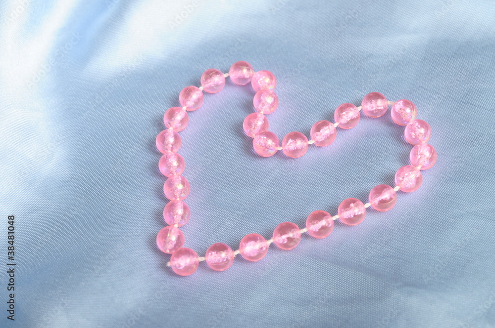 Obraz premium Heart shaped pink pearls child's necklace on blue tissue