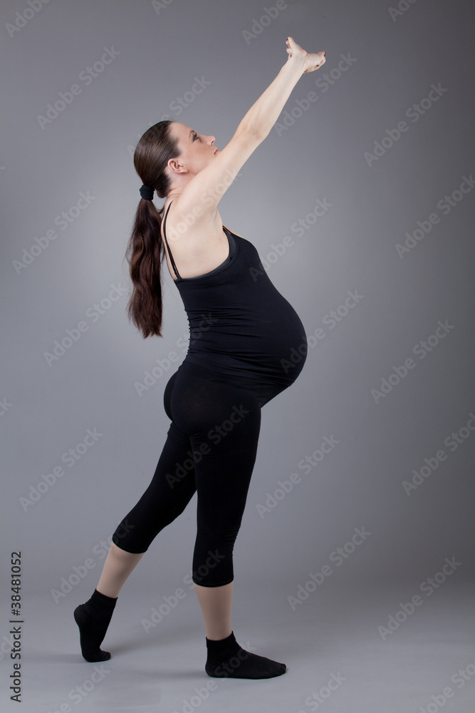 Obraz premium Pregnant woman doing gymnastic exercises on grey background.