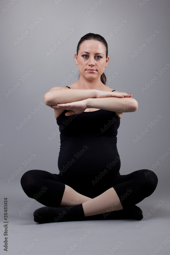 Fototapeta premium Pregnant woman doing gymnastic exercises on grey background.