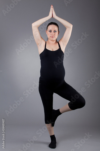 Pregnant woman doing gymnastic exercises on grey background. © EwaStudio