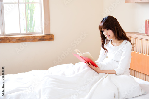 attractive asian woman reading a book on the bed