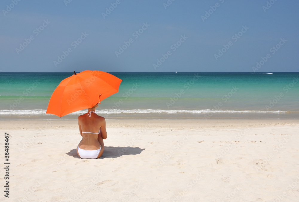 Girl with an orange umbrella on the sandy beach